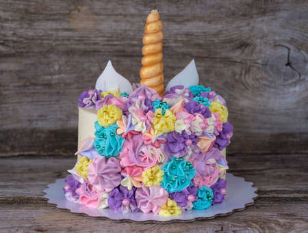 beautiful homemade cake in the form of a unicorn with cream colored flowers on a wooden tableの写真素材