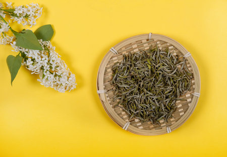 Chinese white tea in bamboo dish and white lilac flowers on yellow background