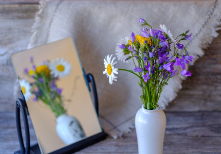 beautiful bouquet of wild flowers of daisies and bells on a wooden table with a reflection in the...