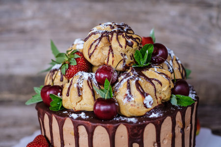 beautiful homemade cake with profiteroles, decorated with strawberries and cherries, on a wooden...
