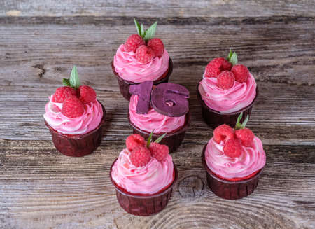 homemade holiday cupcakes with pink cheese cream and raspberry, number sixteen, on wooden backgroundの写真素材
