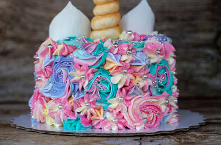 beautiful homemade cake in the form of a unicorn with cream colored flowers on a wooden tableの写真素材