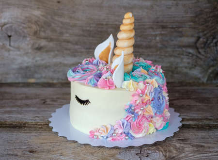 beautiful homemade cake in the form of a unicorn with cream colored flowers on a wooden tableの写真素材