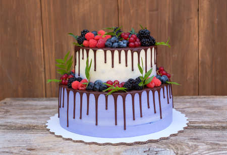 beautiful wedding cake in two tiers, decorated with fresh raspberries, blackberries, blueberries, chocolate icingの写真素材