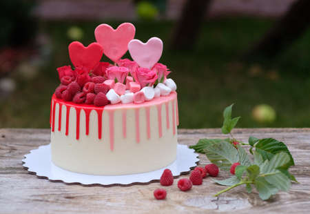 beautiful anniversary cake with pink and red cheese cream, decorated with fresh raspberries, on a wooden tableの写真素材