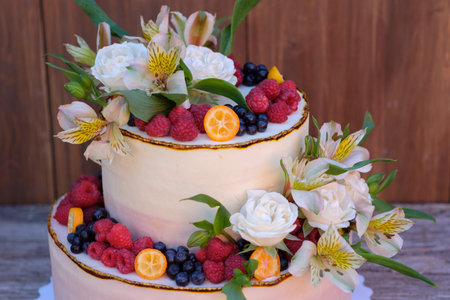 wedding cake in two tiers, decorated with fresh berries and live roses