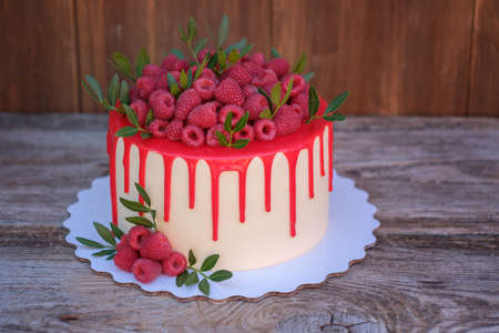 delicate wedding cake with pink frosting, decorated with fresh raspberries, on a wooden backgroundの写真素材