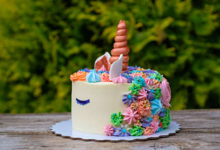 beautiful unicorn cake on green foliage background on wooden tableの写真素材
