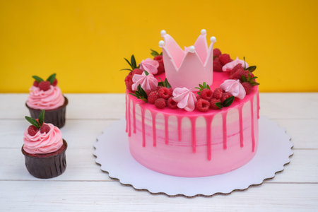 Pink birthday cake decorated with Princess crown, raspberry berries and marshmallow on yellow...
