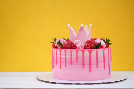 Pink birthday cake decorated with Princess crown, raspberry berries and marshmallow on yellow...