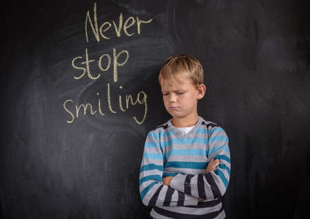 gloomy European boy at the black Board with the inscription " never stop smiling"の写真素材