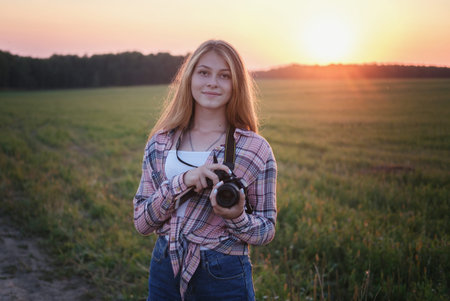 young European girl with a camera in the summer evening at sunset taking pictures