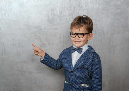 cute European boy in a jacket with a butterfly points his finger at the wall. blank for advertising. isolated gray backgroundのeditorial素材