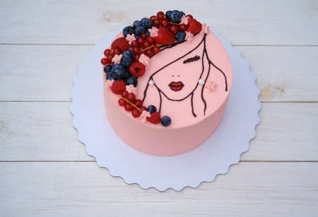beautiful cake with the image of a girl with fresh berries on her hair and delicate pink creamの写真素材