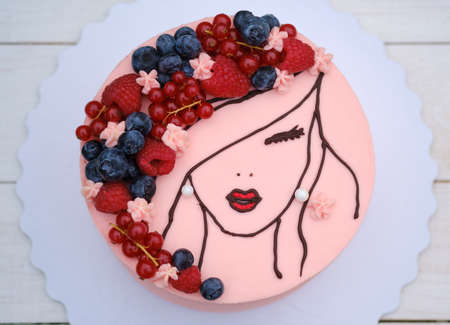 beautiful cake with the image of a girl with fresh berries on her hair and delicate pink creamの写真素材