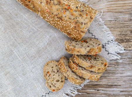 fresh baguette with sesame and red pepper on a linen napkin on a wooden tableの写真素材