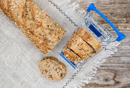 fresh baguette with sesame and red pepper on linen napkin and mini supermarket trolleyの写真素材