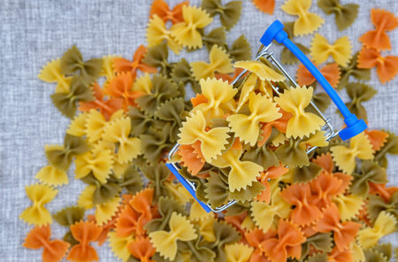 multi-colored pasta in the form of bows in the supermarket cart top view on a gray backgroundの写真素材