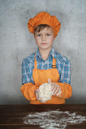 European boy dressed as a cook is engaged in cooking homemade pizza. rolls out the dough, lays out the sausage and tomatoesの写真素材