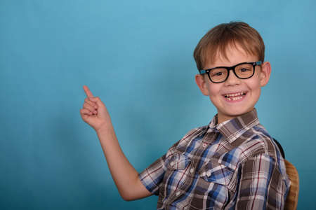 a cute European boy with glasses points his finger at an empty background . blank for design and advertising on blue backgroundの写真素材