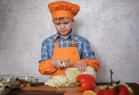 cute European boy cuts Chinese cabbage with knife on cutting Board for vegetable saladの写真素材