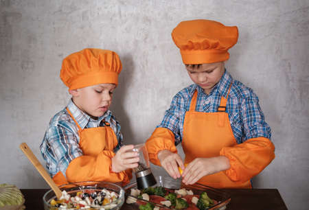 two young chefs in orange suits cook red fish with broccoli and vegetable salad. two brothers of European appearance. family dinner.の写真素材