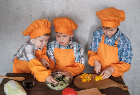 three cute European boys in orange costumes cook prepare a salad of vegetables. cooking a family dinnerの写真素材