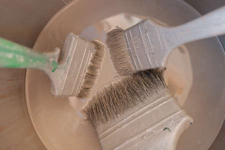 three paint brushes of different sizes in a bucket of paintの写真素材