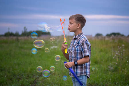 cute European boy blowing big bubbles on a summer evening in nature. children play with soap bubblesの写真素材