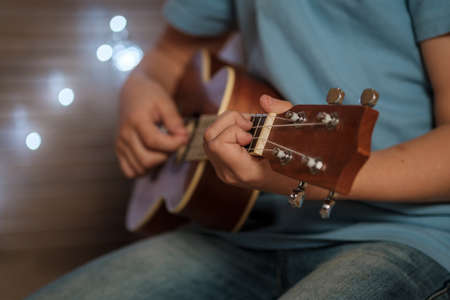 a teenage boy plays the ukulele guitar. hands with guitar close up without faceの写真素材