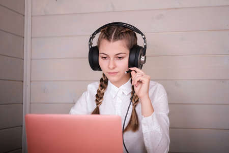 beautiful young girl in headphones in front of a laptop monitor. online study at home during the period of quarantine and the covid-19 coronavirus pandemicの写真素材