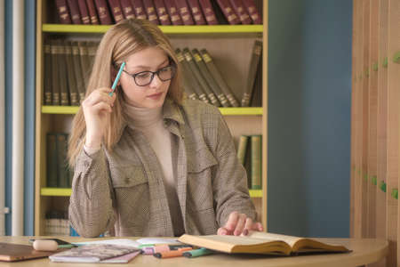 young beautiful girl student works with books in the library. preparation for exams in the library against the background of bookshelvesの写真素材