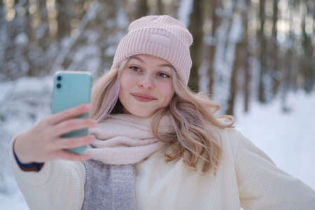 young beautiful woman takes a selfie on a smartphone camera in a snowy parkの写真素材