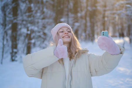 young beautiful girl talking with friends using video communication in a beautiful winter forestの写真素材