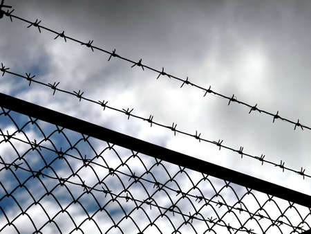 Barbed wire fence with dark clouds in background - imprisonment concept     の写真素材