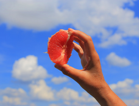 The woman's hands hold a grapefruit against the sky and clouds. A close-up photo.の写真素材