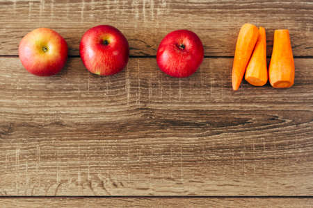 red apple and yellow carrots on the wooden table, live food, helpfulの写真素材