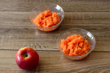Carrot-apple puree in a glass container on a wooden tableの写真素材