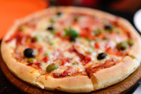 Pizza with ham, pepper and olives on a wooden board