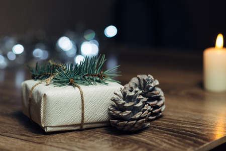 Burning candle on a table with Christmas decorations pine cones and a box on the background of garlands,の写真素材