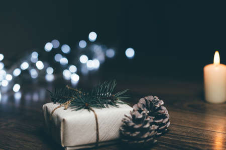 Burning candle on a table with Christmas decorations pine cones and a box on the background of garlands,の写真素材