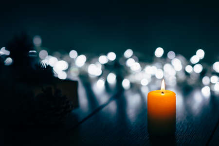 Burning candle on a table with Christmas decorations pine cones and a box on the background of garlands,の写真素材