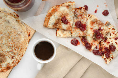 pancakes with strawberry jam and black coffee on a wooden boardの写真素材