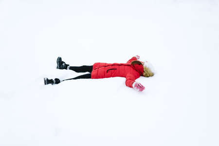 girl in a red jacket in winter, lying in the snowの写真素材