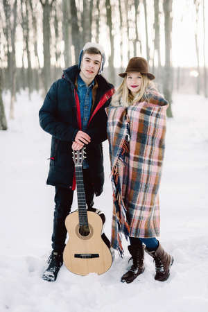 A man with a guitar, holding hands with his girlfriend atmospheric sensual moment. Stylish hipster couple in trendy look. rustic wedding concept, winter forest.の写真素材