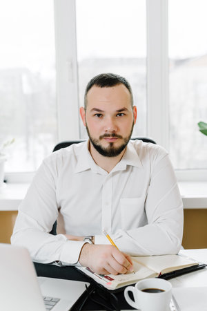 bearded businessman in a white shirt at a desk, working at the computer