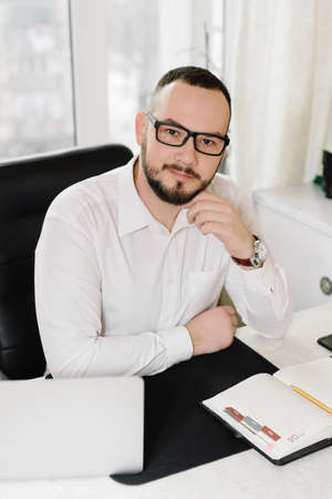 bearded businessman in a white shirt at a desk, working at the computerの写真素材