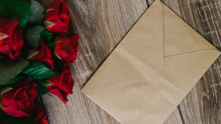 Bouquet of red roses on a wooden table with an envelope and a blank paper card for your text, concept praznikiの写真素材