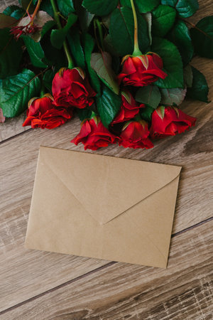 Bouquet of red roses on a wooden table with an envelope and a blank paper card for your text, concept praznikiの写真素材