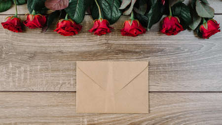 Bouquet of red roses on a wooden table with an envelope and a blank paper card for your text, concept praznikiの写真素材